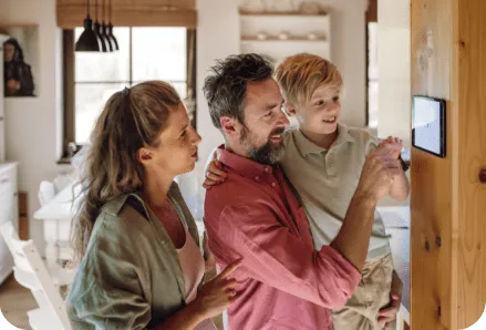 Family interacting with a wall-mounted energy monitoring screen, showing electrical meter use